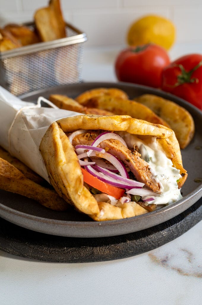 A gyro sandwich on a gray plate surrounded by fries.