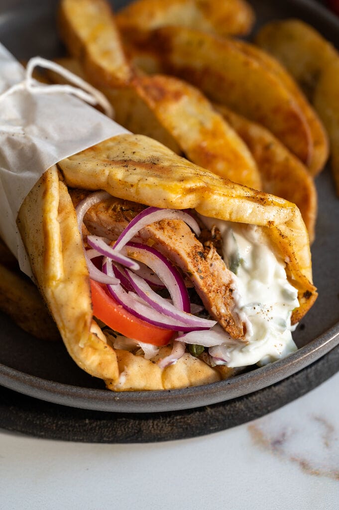 A gyro sandwich on a gray plate surrounded by fries.