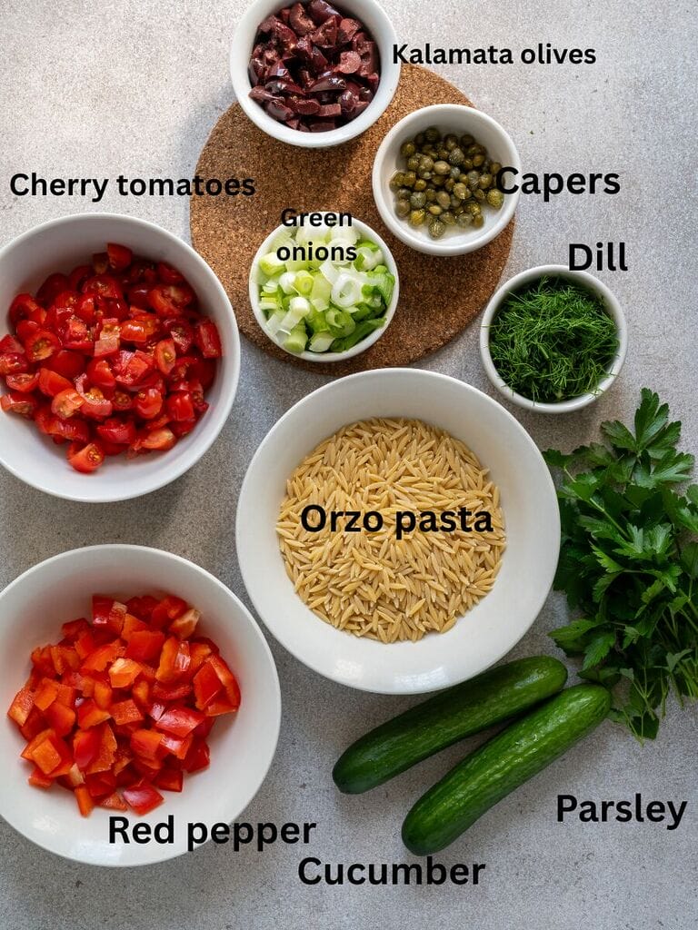 Ingredients for the salad which include: Orzo pasta, cherry tomatoes, red pepper, cucumber, green onions, kalamata olives, capers, dill, and parsley.