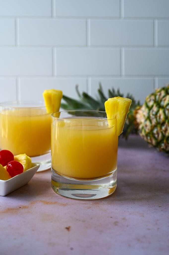 Ouzo pineapple cocktail in a glass topped with a fresh piece of pineapple.