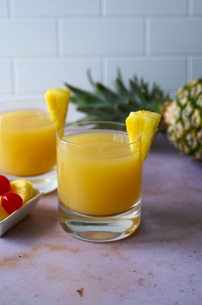 Ouzo pineapple cocktail in a glass topped with a fresh piece of pineapple.