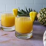 Ouzo pineapple cocktail in a glass topped with a fresh piece of pineapple.