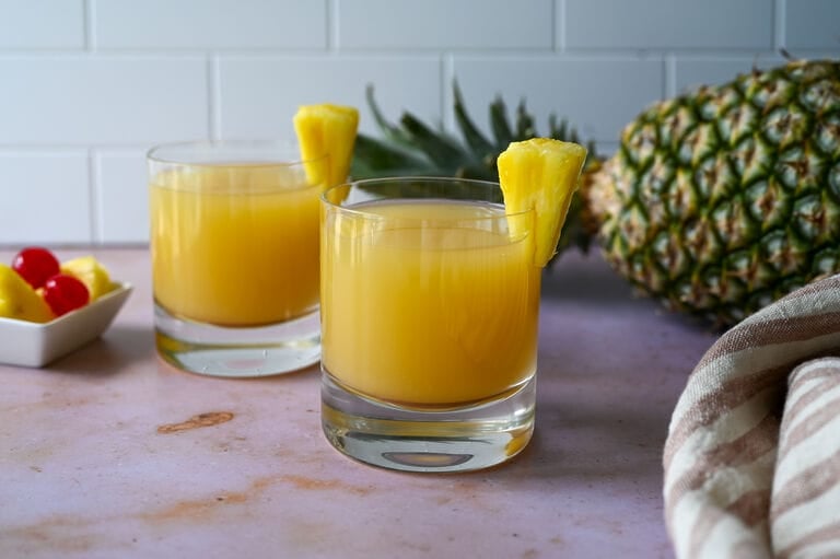 Ouzo pineapple cocktail in a glass topped with a fresh piece of pineapple.