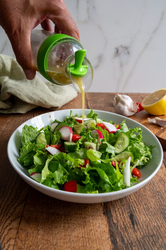 Pouring the Greek salad dressing over the salad.
