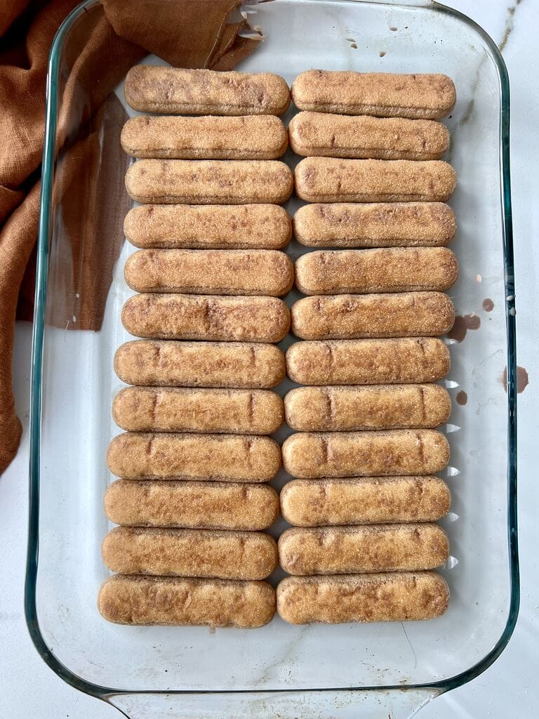 Layering the ladyfingers in a pyrex pan.