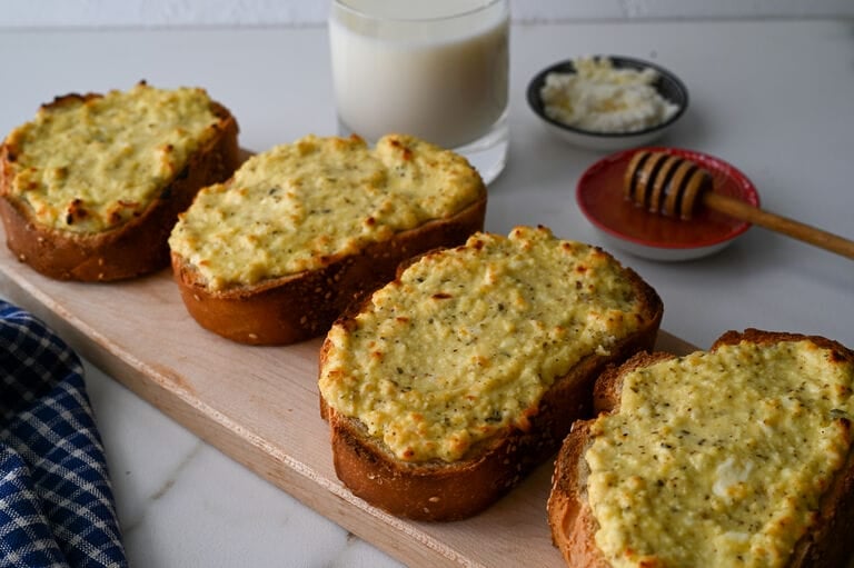 Greek cheese topped bread on a wooden platter.