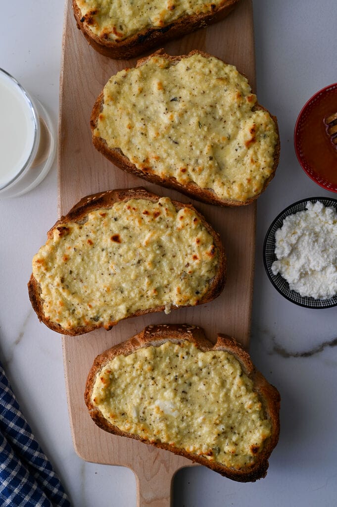 Greek cheese topped bread on a wooden platter.