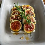 Baked Greek feta with figs in a small white casserole dish, topped with honey and rosemary.