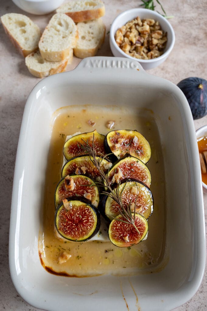 Baked Greek feta with figs in a small white casserole dish, topped with honey and rosemary.