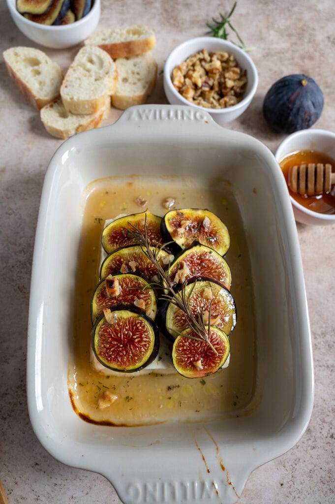 Baked Greek feta with figs in a small white casserole dish, topped with honey and rosemary.