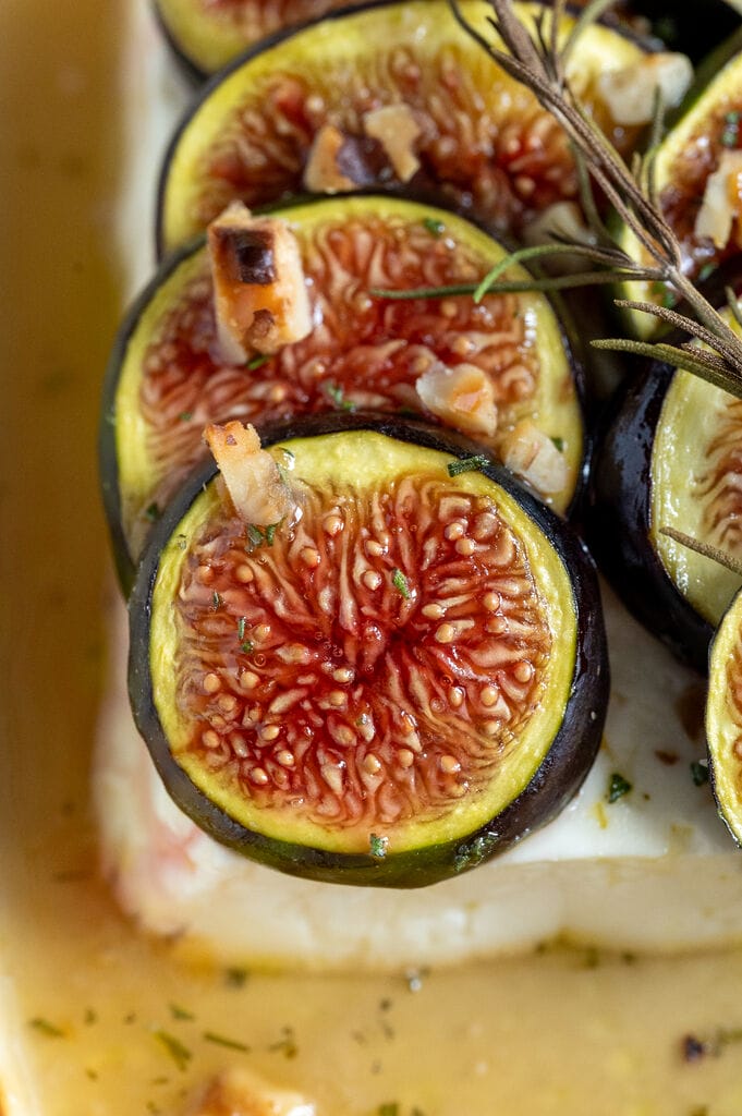 Baked Greek feta with figs in a small white casserole dish, topped with honey and rosemary.