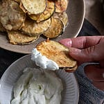 Fried eggplant chips on a brown plate surrounded by tzatziki.