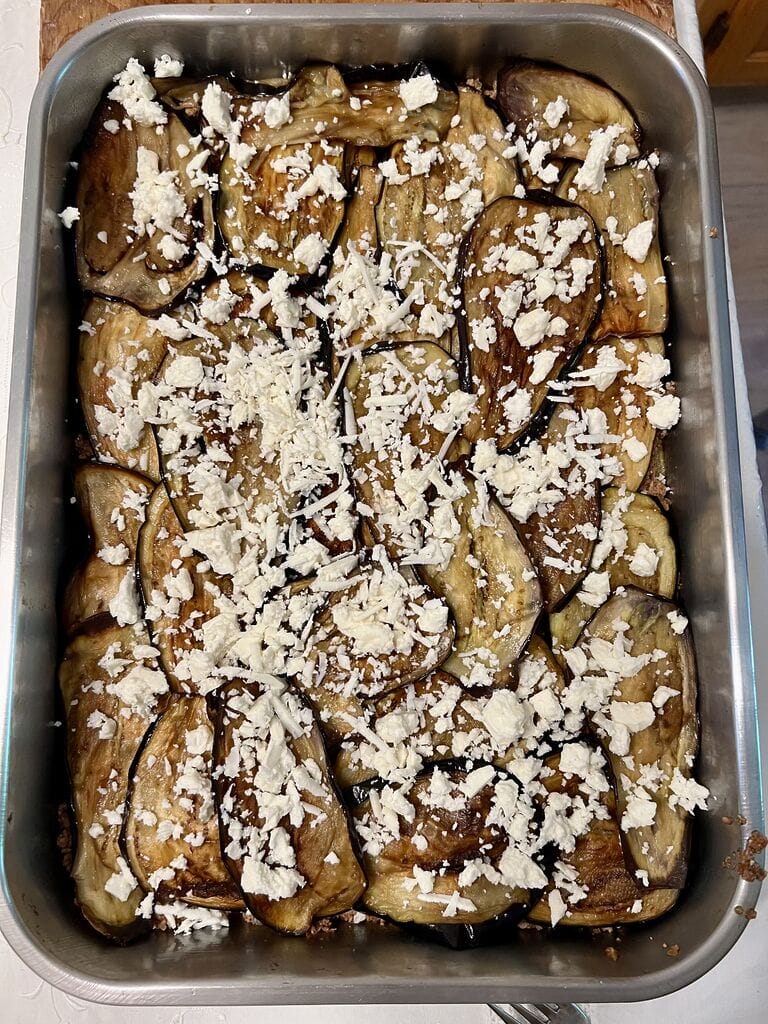 Sprinkling feta on top of eggplant.