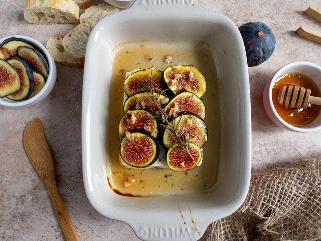 Baked Greek feta with figs in a small white casserole dish, topped with honey and rosemary.