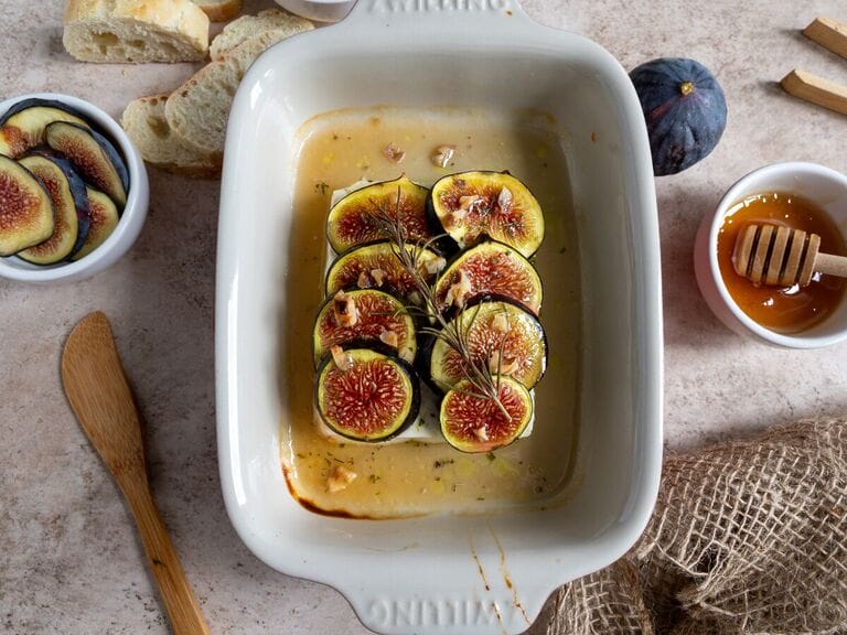 Baked Greek feta with figs in a small white casserole dish, topped with honey and rosemary.