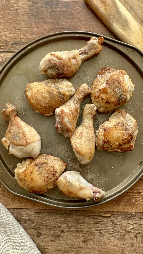 The browned chicken pieces on a round baking sheet.