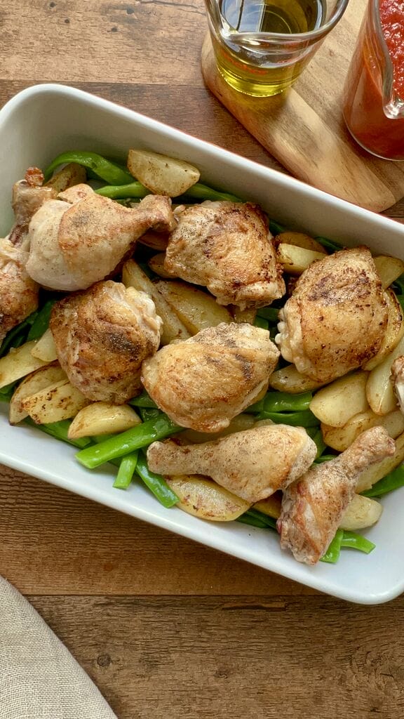 The green beans and potatoes and chicken in a white casserole dish.