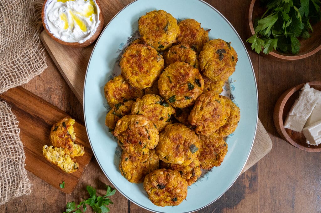 Baked squash fritters with feta on a white platter.