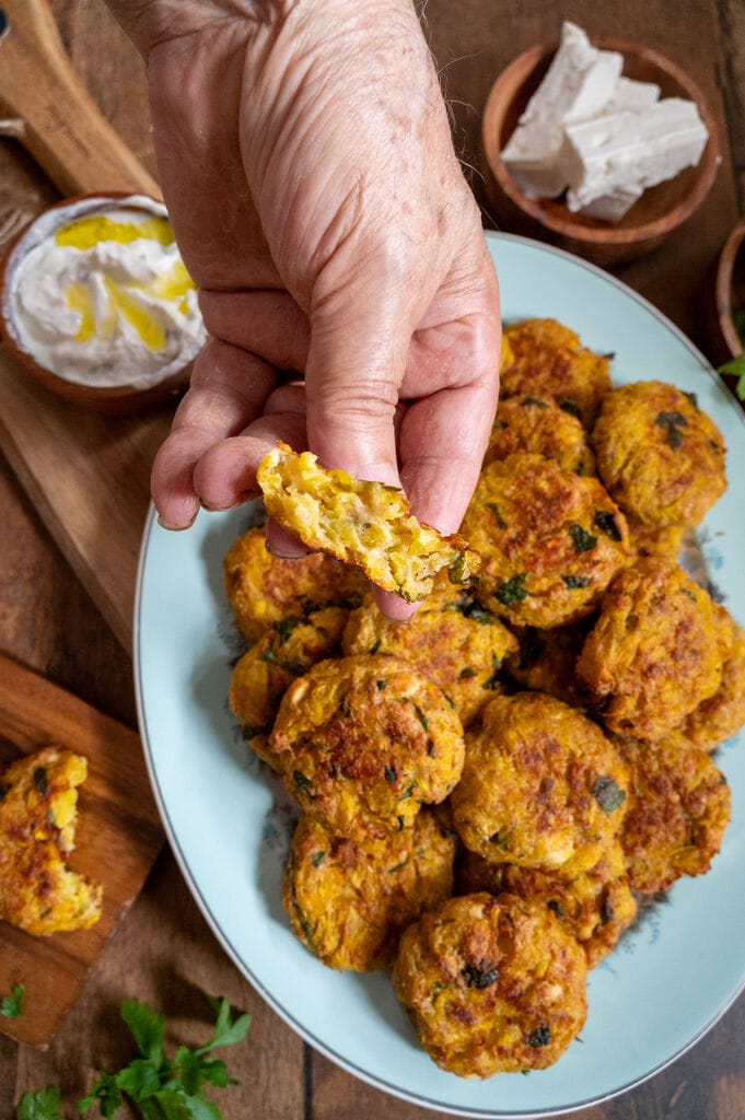 Baked squash fritters with feta on a white platter. Showing the inside of one.