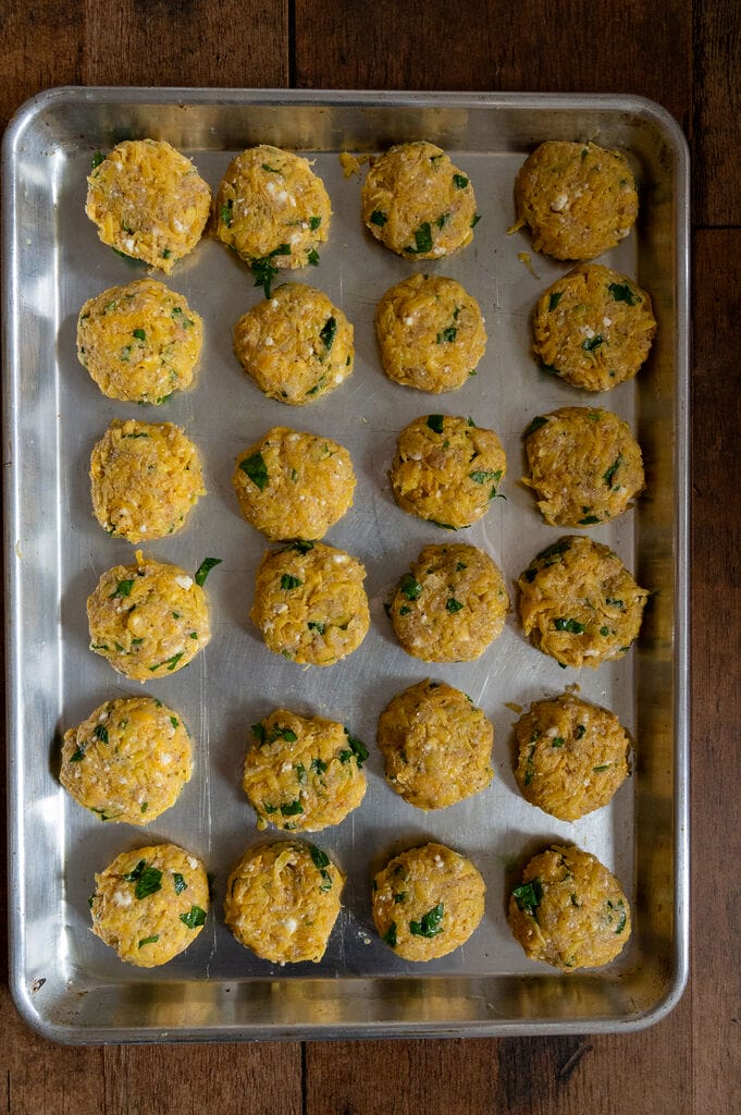 Squash fritters with feta on a parchment lined baking sheet ready to bake.