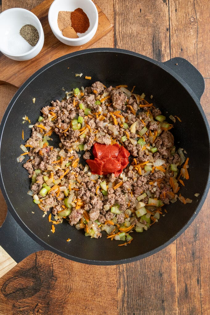 adding the tomato paste to the ground beef, celery, and carrot and onion mixture.