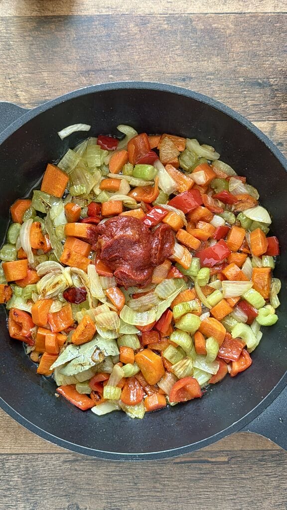 Adding the tomato paste in the frying pan with the caramelized veggies.