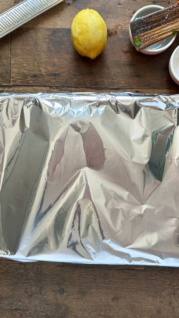 Greek Baked Gigantes with Sausage (Loukaniko), in a roasting pan ready to go in oven and covered in foil.