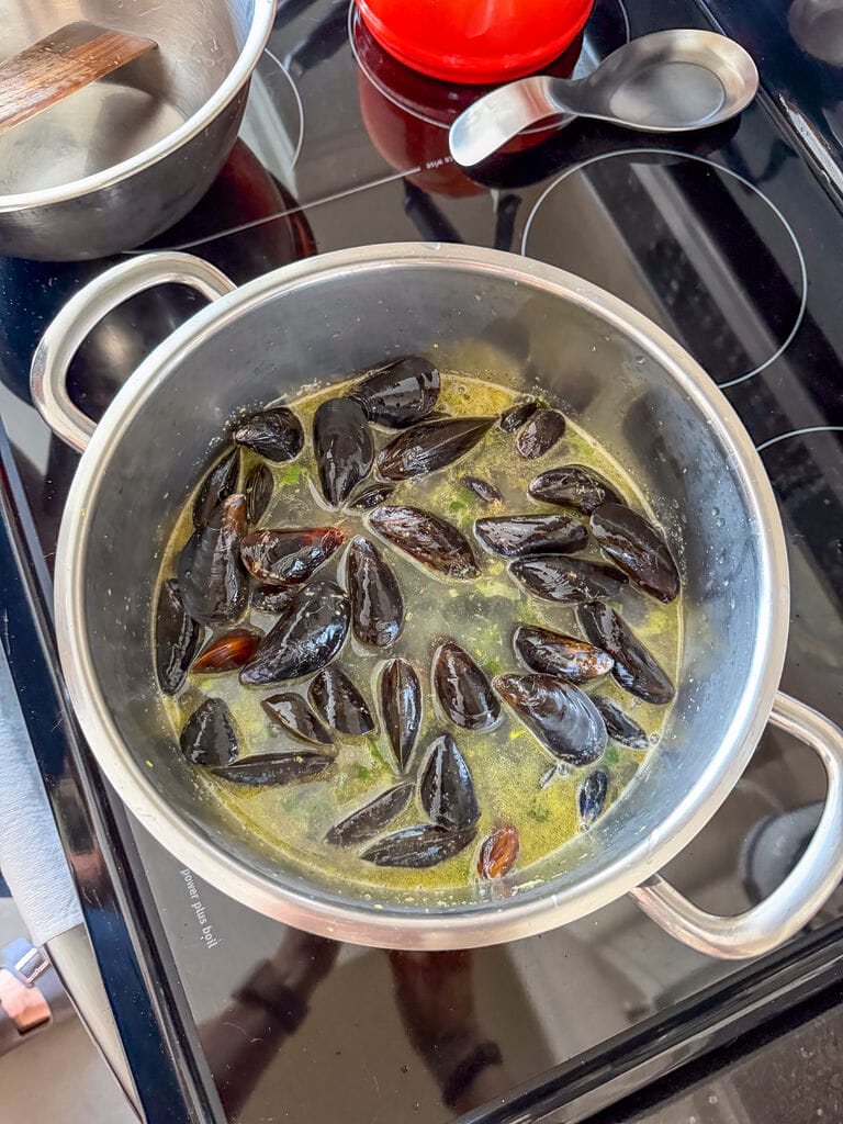 Adding the mussels to the sauce pot with the liquid and veggies.