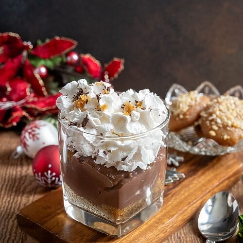 Greek melomakarona chocolate pudding in a glass tumbler, topped with whipped cream.