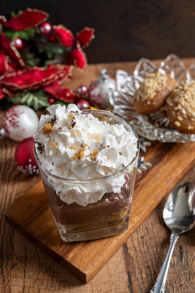 Greek melomakarona chocolate pudding in a glass tumbler, topped with whipped cream.