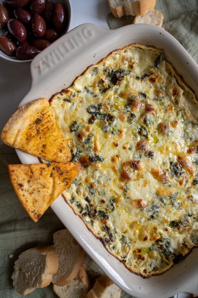 Baked spanakopita dip in a white casserole dish, with 2 baked pita chips on it.