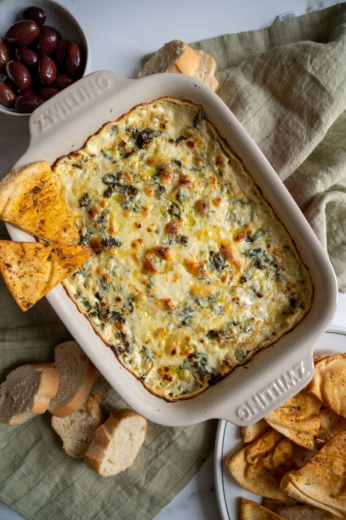 Baked spanakopita dip in a white casserole dish, with 2 baked pita chips on it.