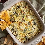 Baked spanakopita dip in a white casserole dish, with 2 baked pita chips on it.
