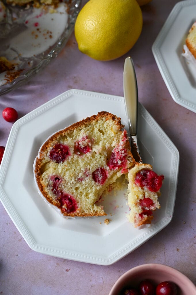 A piece of lemon and cranberry olive oil cake on a white plate.