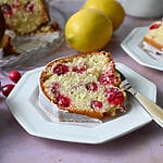 A piece of lemon and cranberry olive oil cake on a white plate.