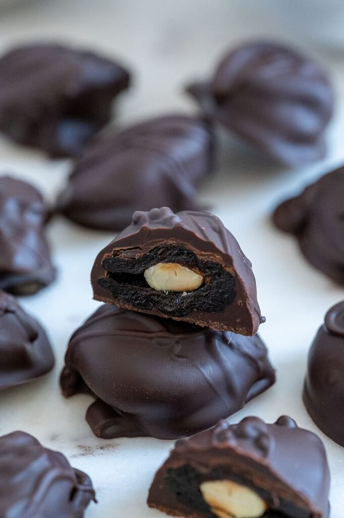 Chocolate covered prunes with almonds on a white plate.