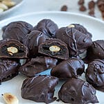 Chocolate covered prunes with almonds on a white plate.