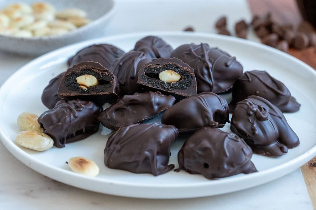 Chocolate covered prunes with almonds on a white plate.
