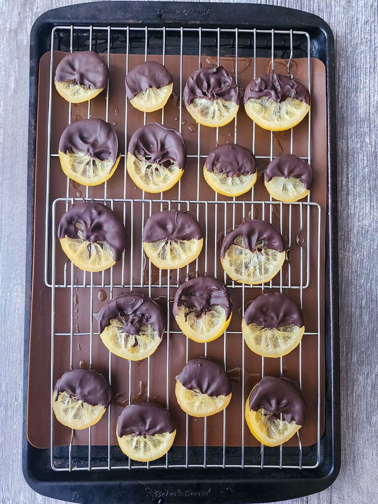 Candied lemon slices half dipped in dark chocolate on a wire rack.