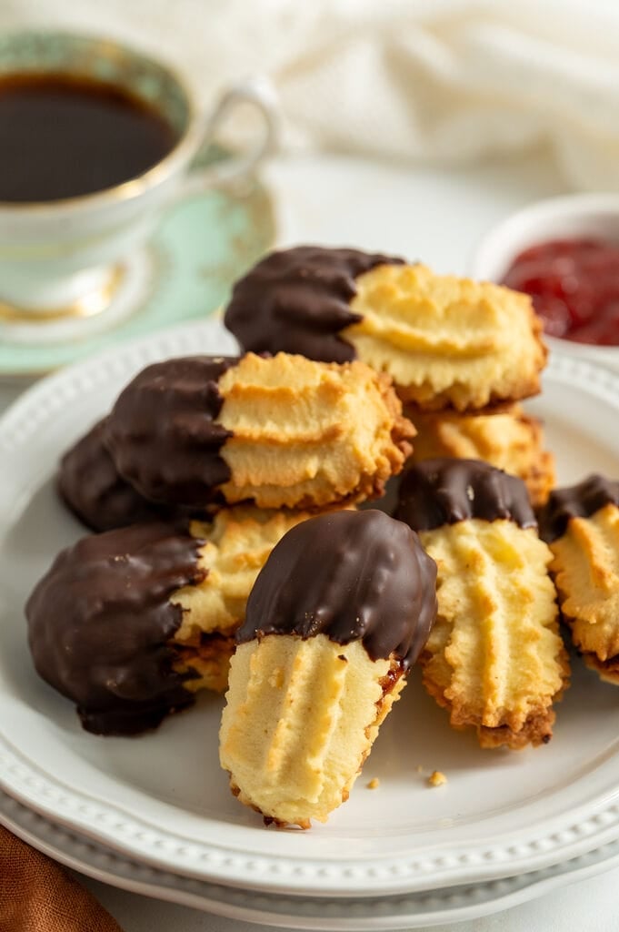 Cookies stacked on a white plate, surrounded by coffee, and jam.