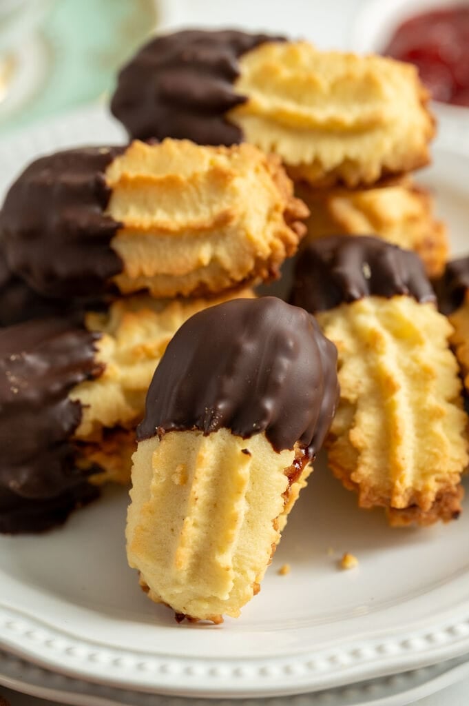 Cookies stacked on a white plate, surrounded by coffee, and jam.