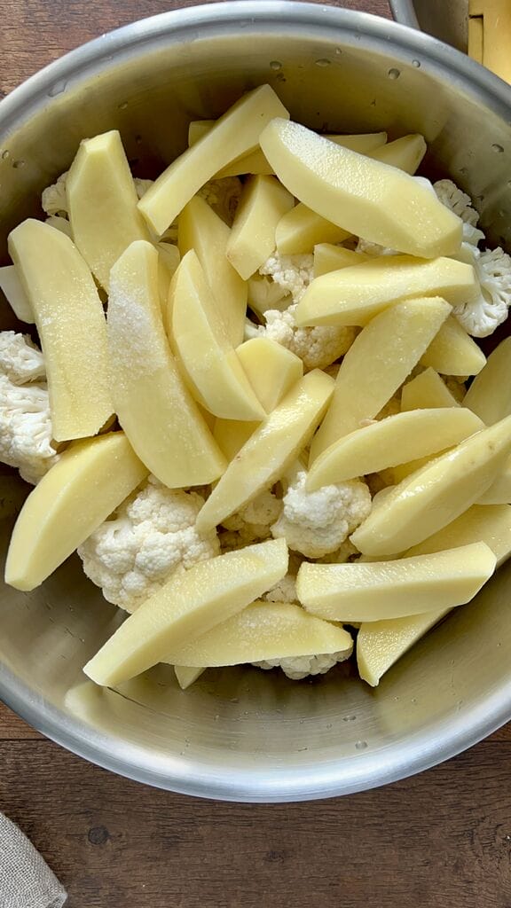 Adding salt to the potatoes and cauliflower.
