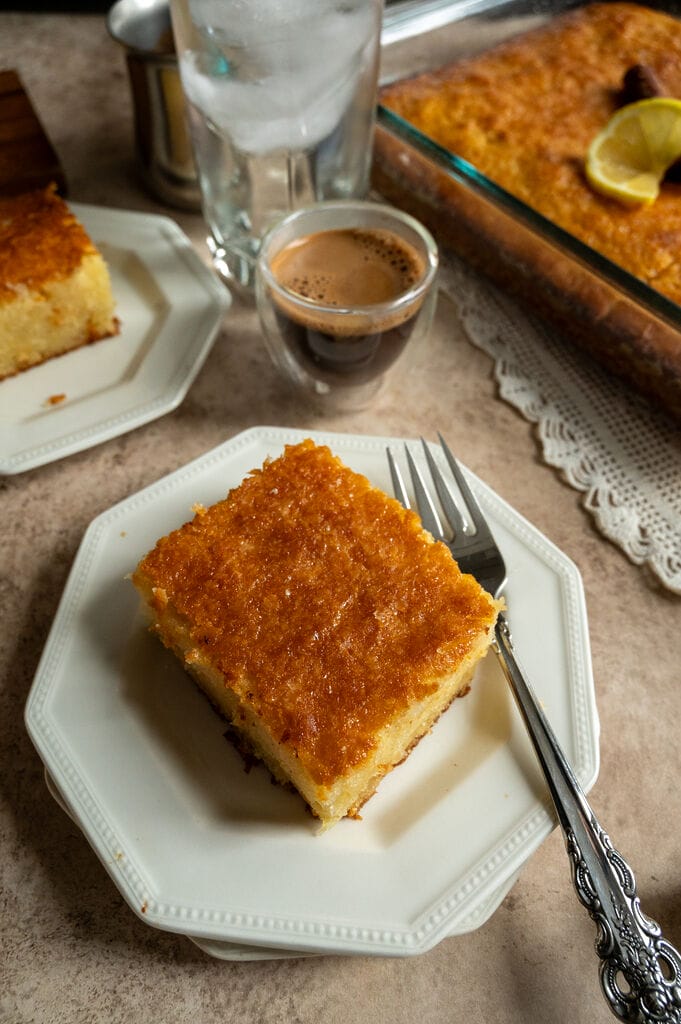 A piece of lemonopita cake on a white plate, with a Greek coffee next to it.