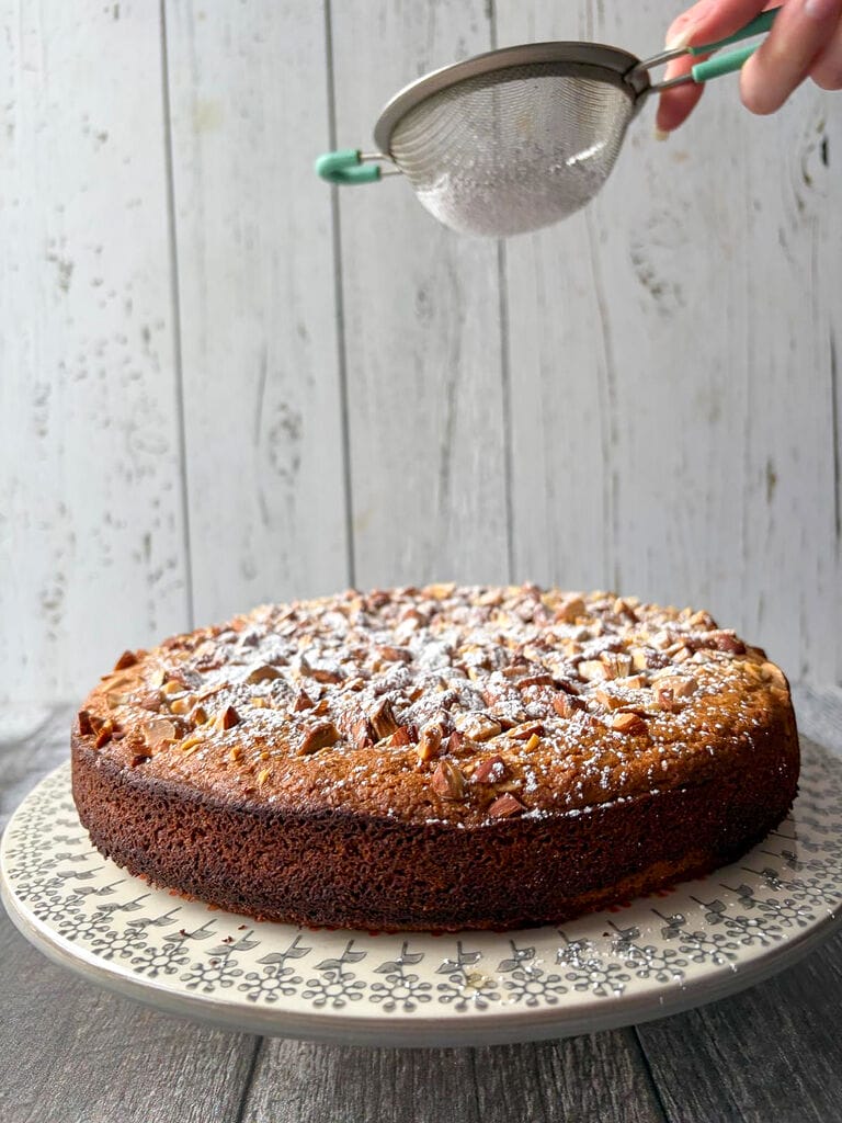 The cake plated on a beautiful platter being sprinkled with icing sugar.