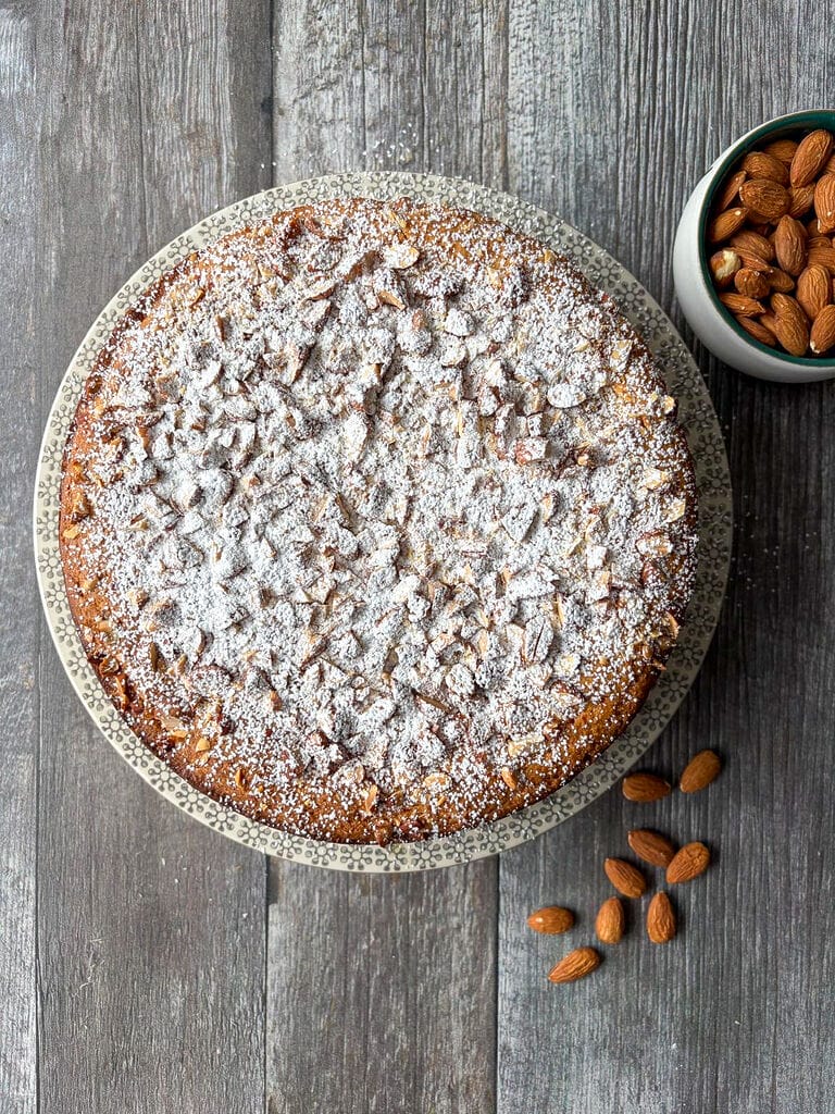 The cake plated on a beautiful platter surrounded by almonds.