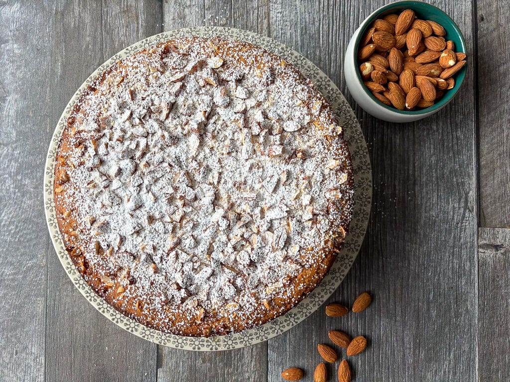 The cake plated on a beautiful platter surrounded by almonds.