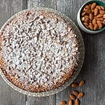 The cake plated on a beautiful platter surrounded by almonds.