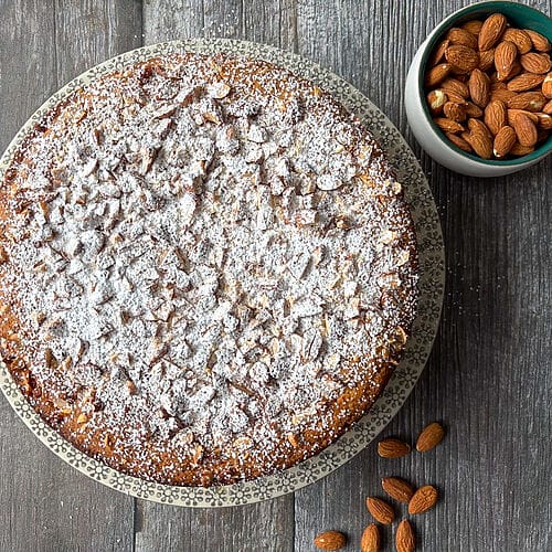 The cake plated on a beautiful platter surrounded by almonds.