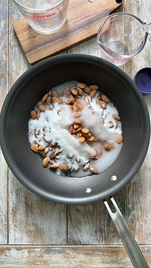 Adding the sugar and water to the almonds in frying pan.