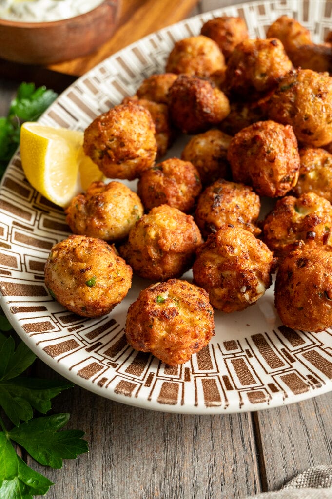 Greek chicken meatballs with feta on a white and brown platter, surrounded by lemons, tzatziki and olives.